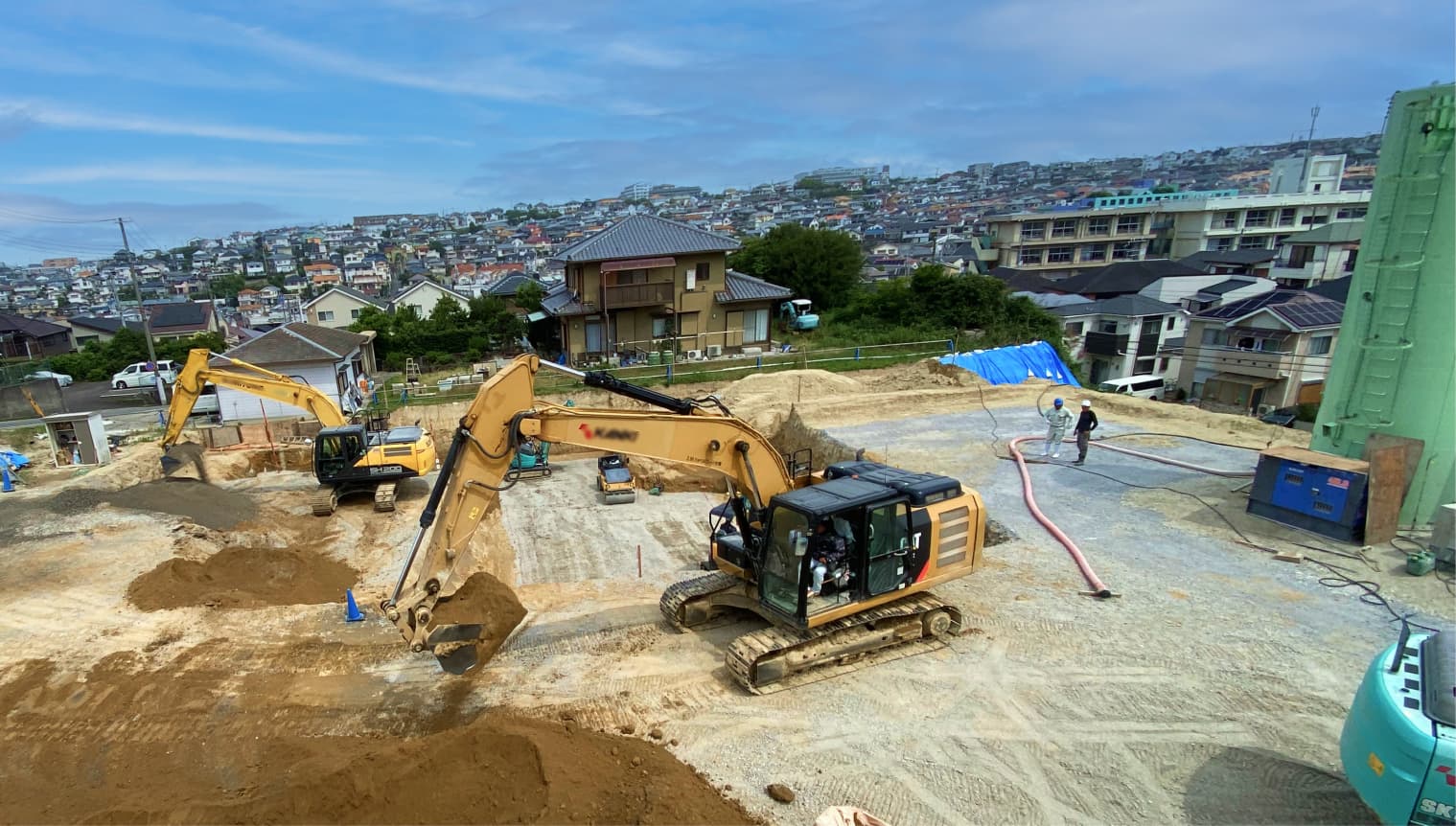 住宅街に隣接する造成現場で複数の重機が土砂を掘削・整地する様子