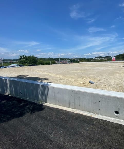 更地となった広い造成地と手前に設けられたコンクリート擁壁の施工